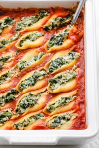 side angle view of vegan stuffed shells in a baking dish with items surrounding.