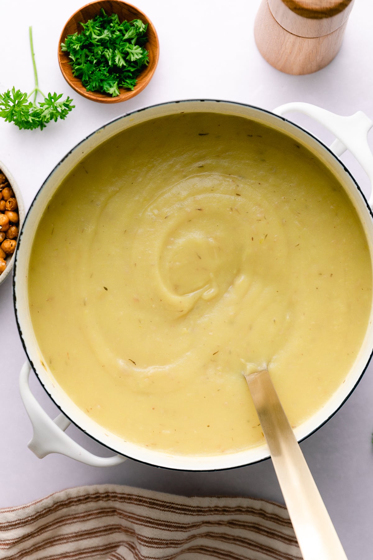 top down view of freshly pureed vegan potato leek soup in a pot with items surrounding.