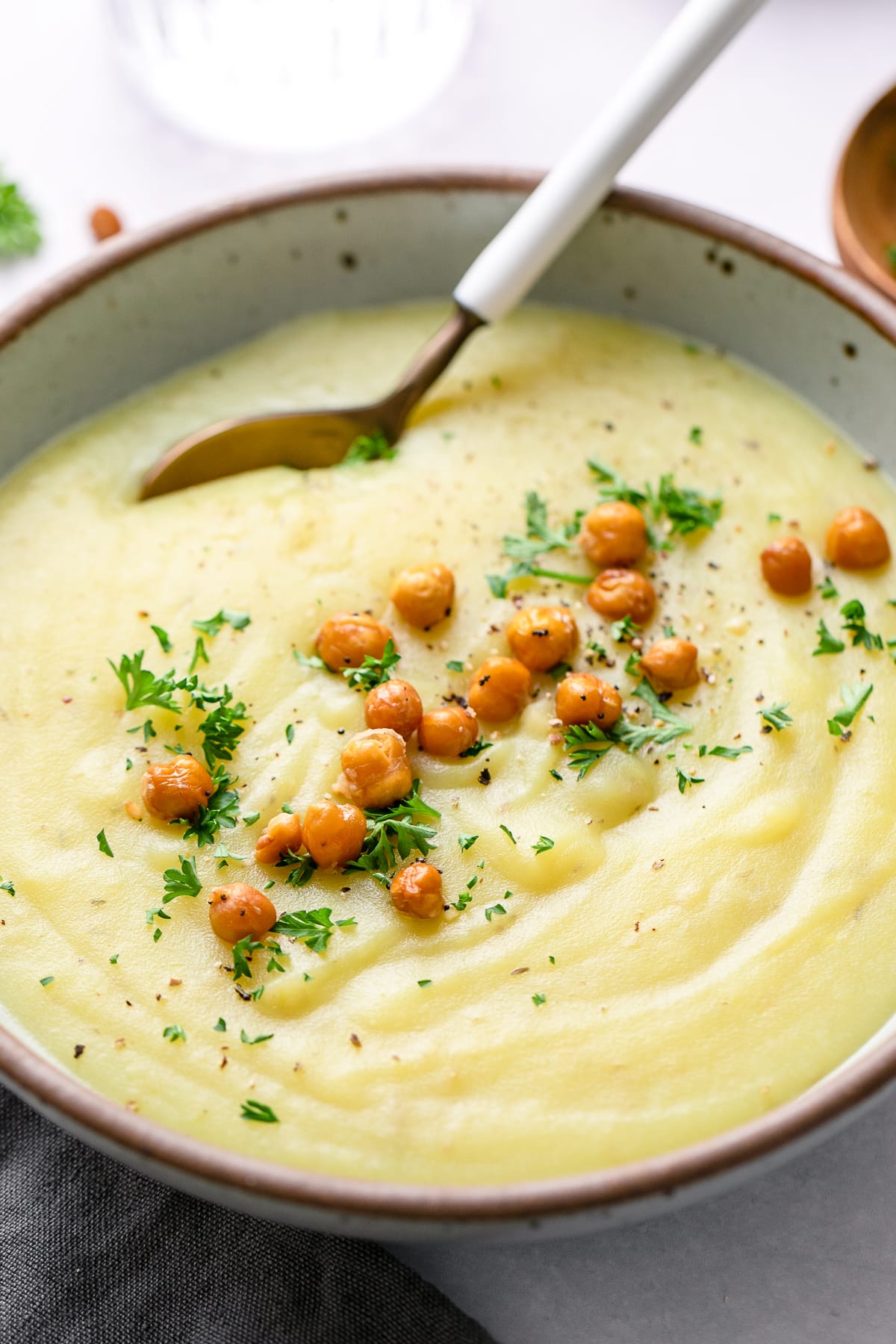 side angle view of creamy vegan potato leek soup in a bowl with items surrounding.