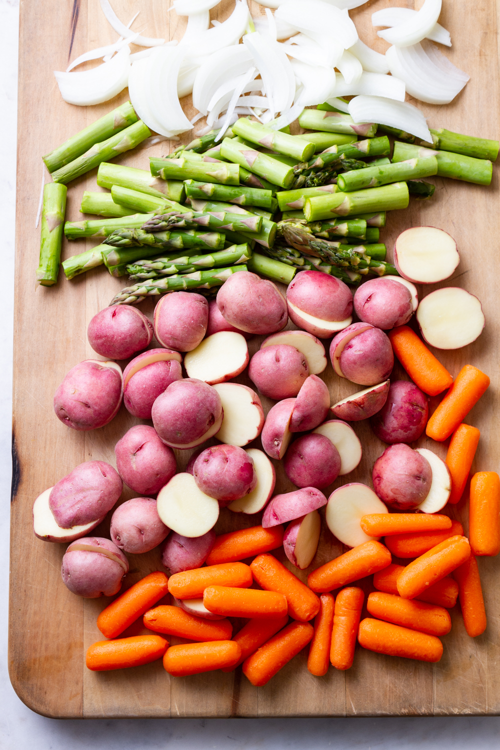 prepped carrots, asparagus, red potatoes and onion on a cutting board