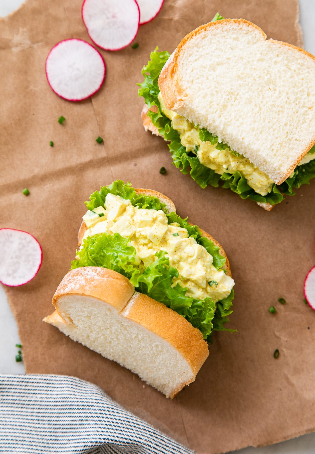 top down view of two halves of vegan egg salad sandwich on brown paper with items surrounding.