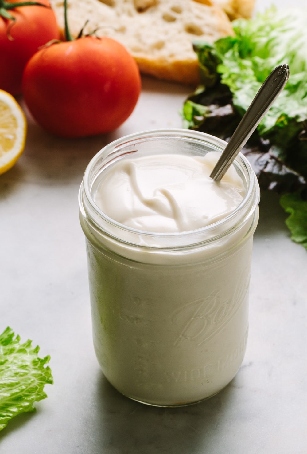 thick and creamy vegan mayo in a mason jar with knife on marble countertop