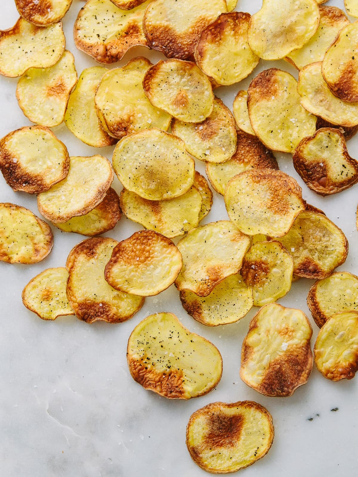 top down view of homemade baked potato chips on a marble slab.