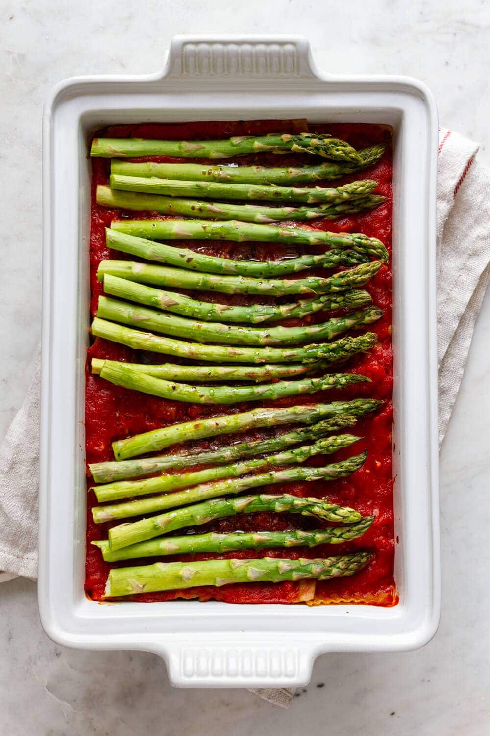 top down view of a white baking dish with assemble and cooked vegan lasagna baked with fresh asparagus on top