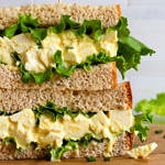 head on view of vegan egg salad sandwich with leafy greens sliced in half and stacked.