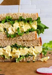 head on view of vegan egg salad sandwich with leafy greens sliced in half and stacked.