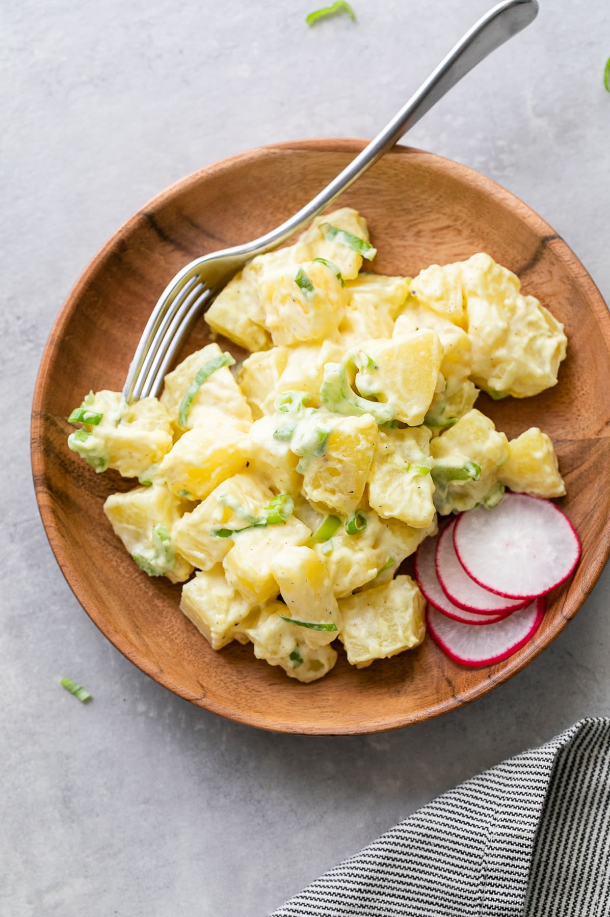 top down view of serving of vegan potato salad on a small wooden plate.