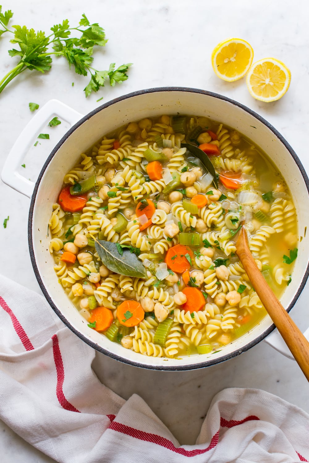 top down view of a big pot of homemade vegan chickpea noodle soup with wooden spoon.