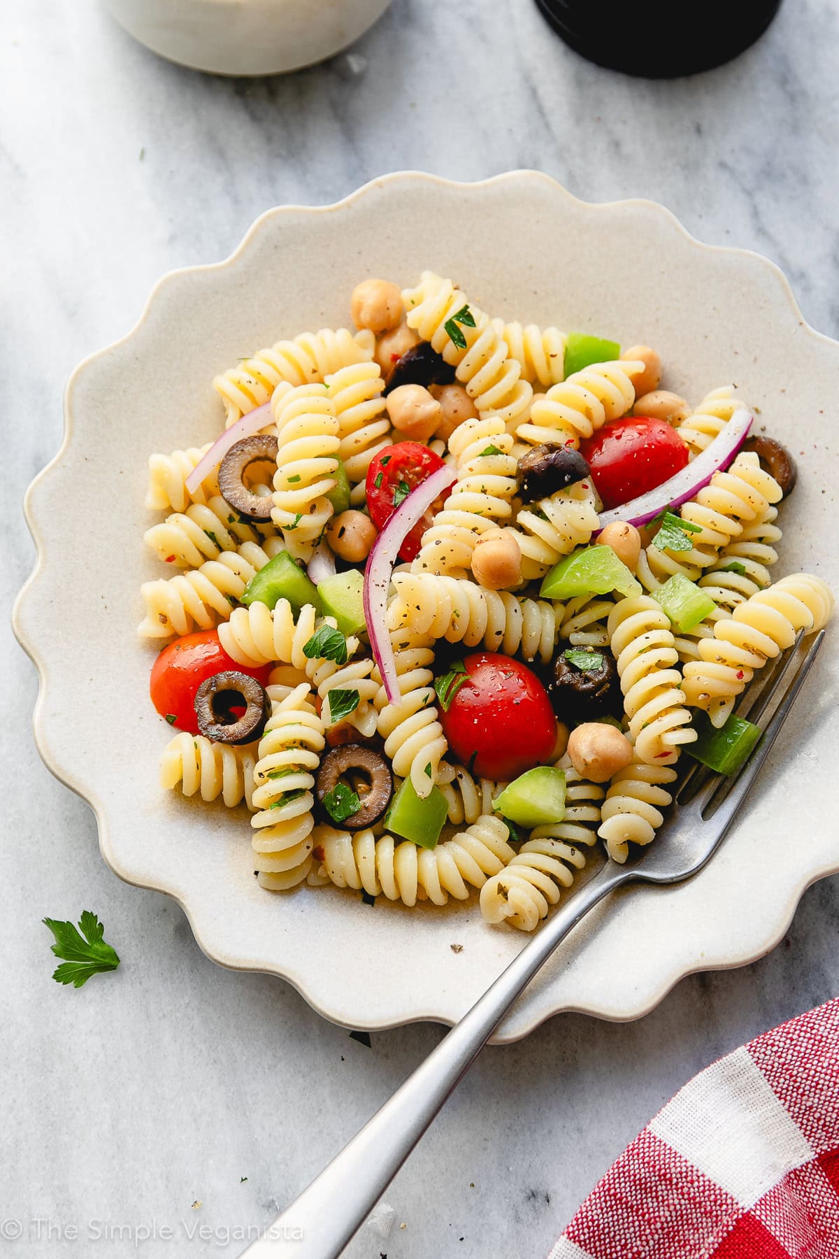 side angle view of plated serving of vegan pasta salad with items surrounding.