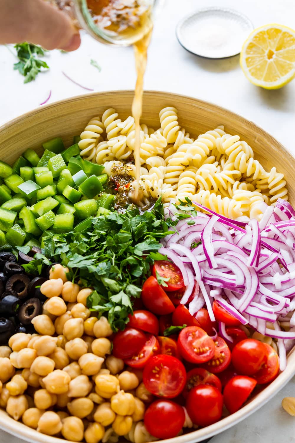 side angle view of ingredients for vegan pasta salad added to a large mixing bowl and dressing being poured overtop.