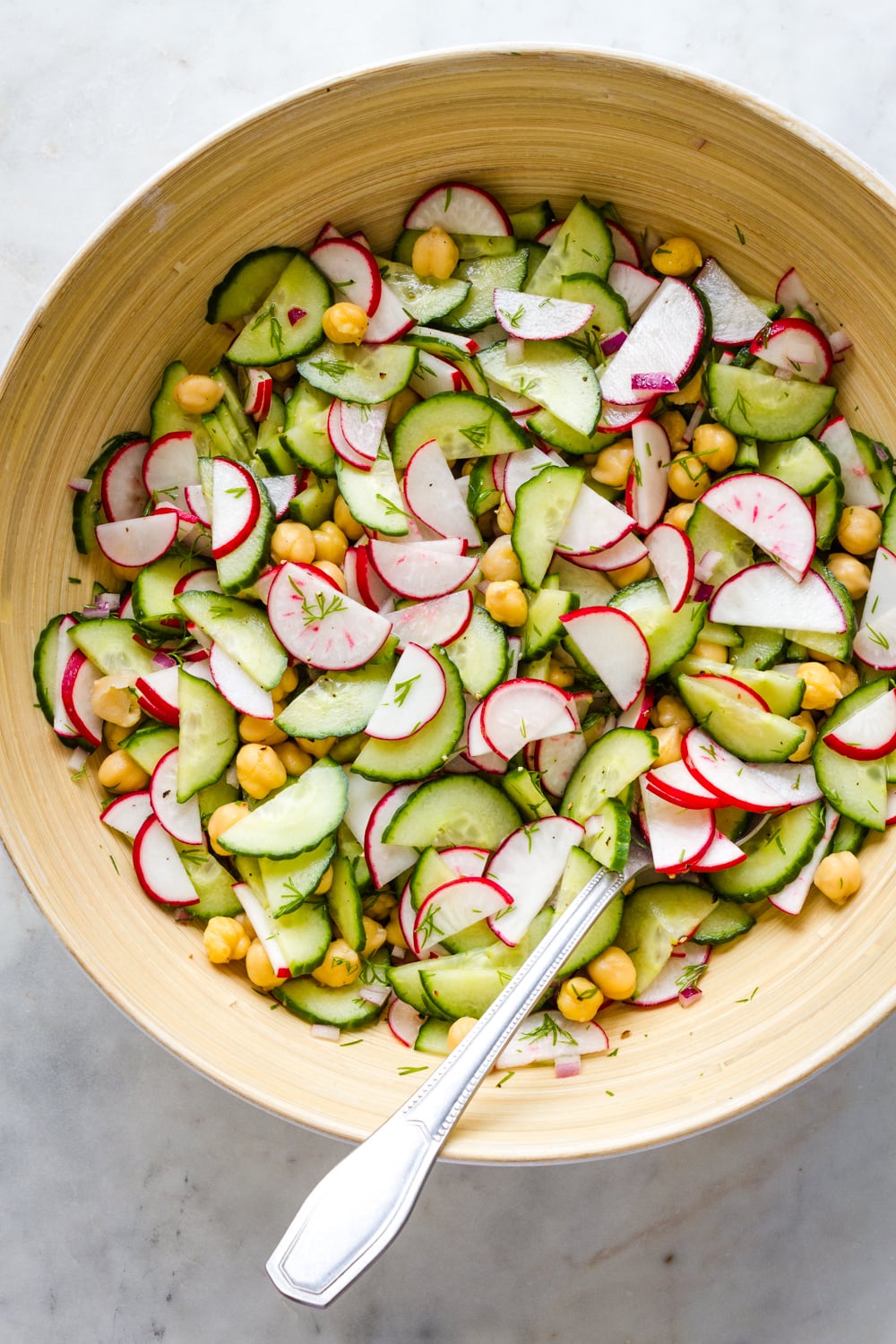 top down view of freshly mixed radish and cucumber salad with a serving spoon on a marble slab