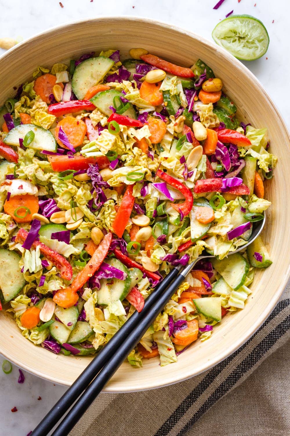 top down view of a large serving bowl with mixed thai crunch salad and stainless steel salad utensils with black handles