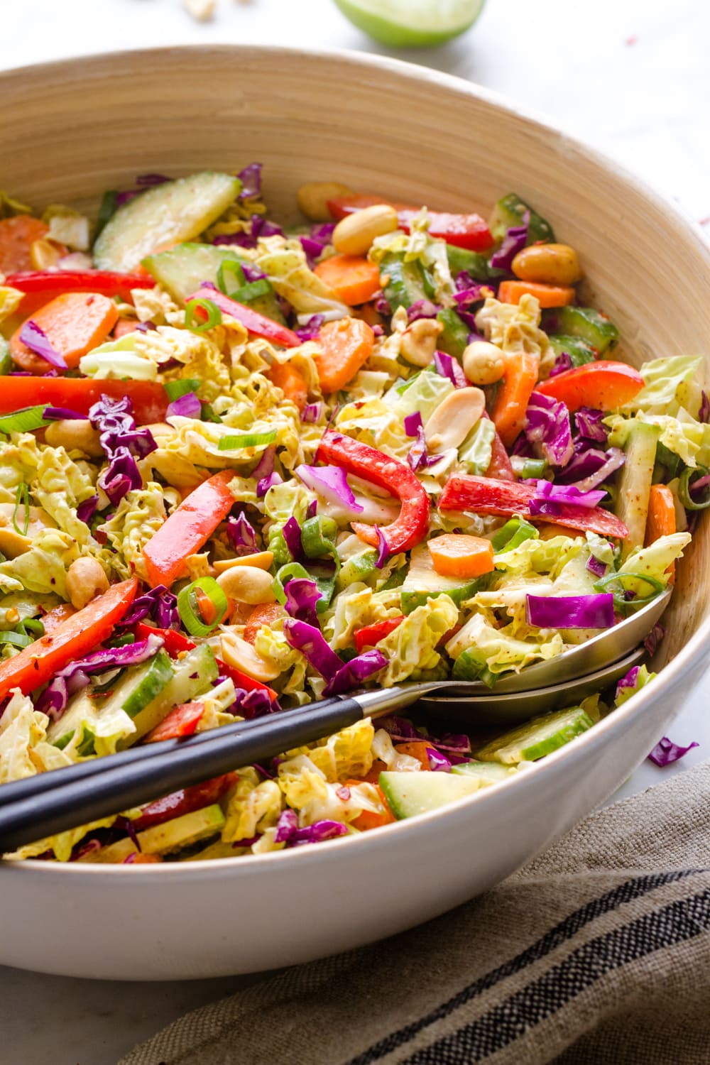 side angle view of freshly mixed thai crunch salad in a bamboo bowl with salad serving utensils