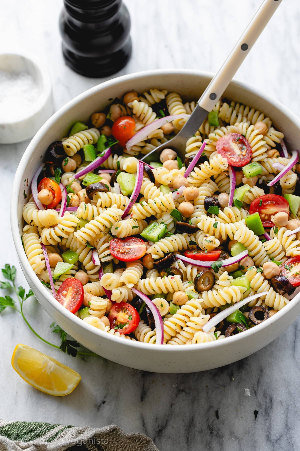 side angle view of freshly made pasta salad in a large bowl with spoon and items surrounding.