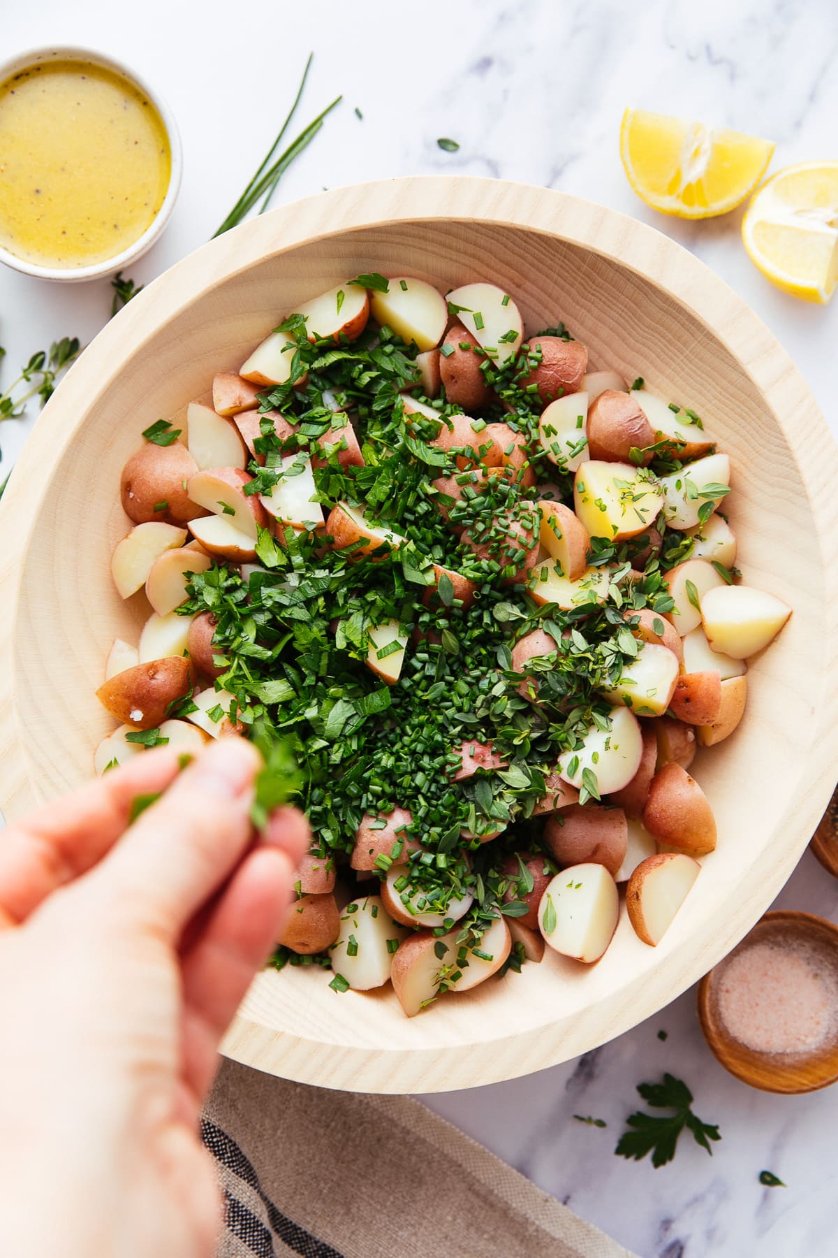 top down view of fresh herbs being added to a bowl with cooked potatoes.