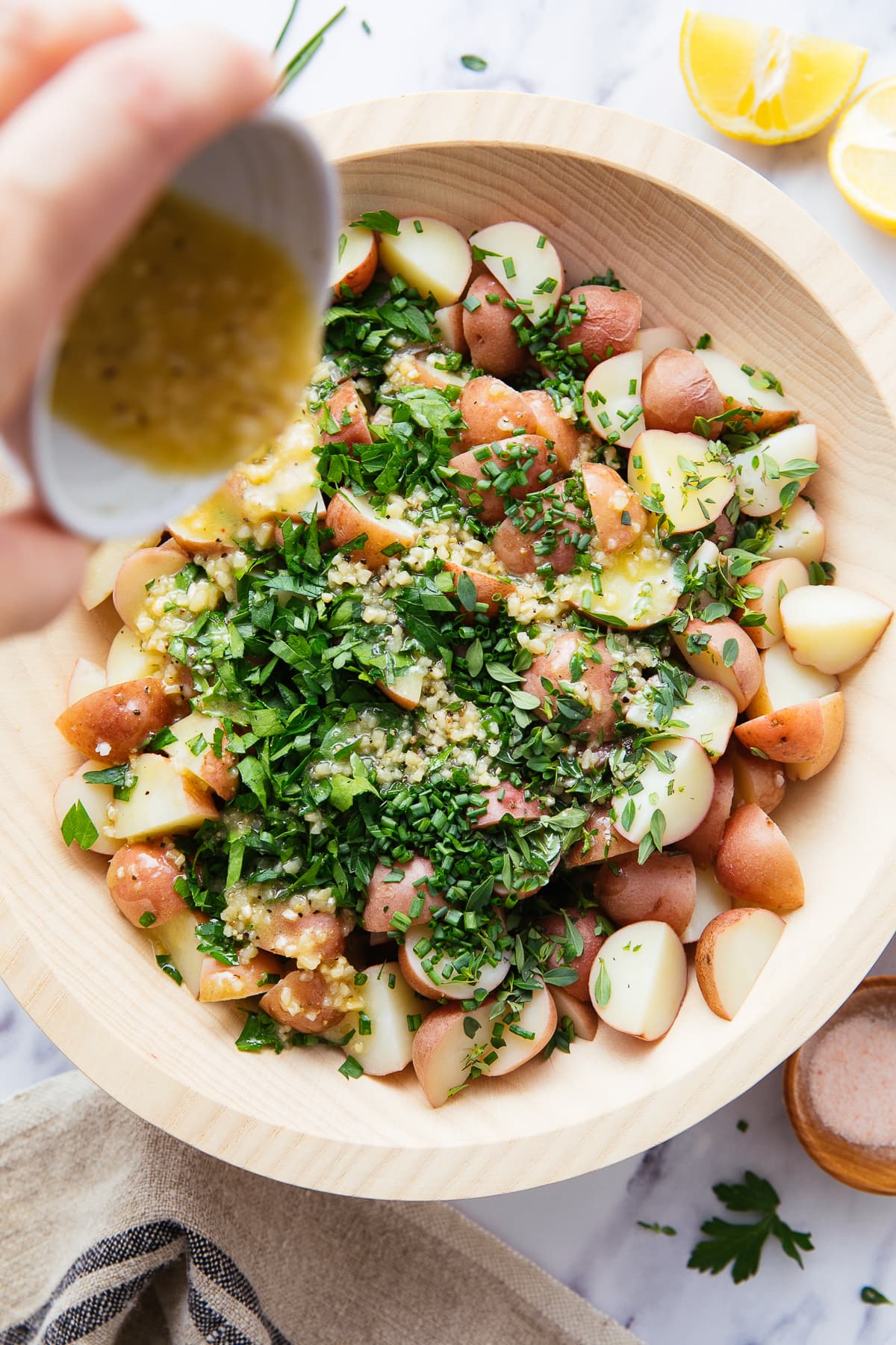 top down view of garlic-dijon dressing with lemon being poured overtop cooked potatoes and fresh herbs.