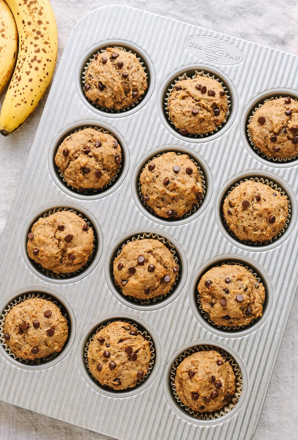 top down view of vegan banana chocolate chip muffins just pulled from the oven in a muffin tin.