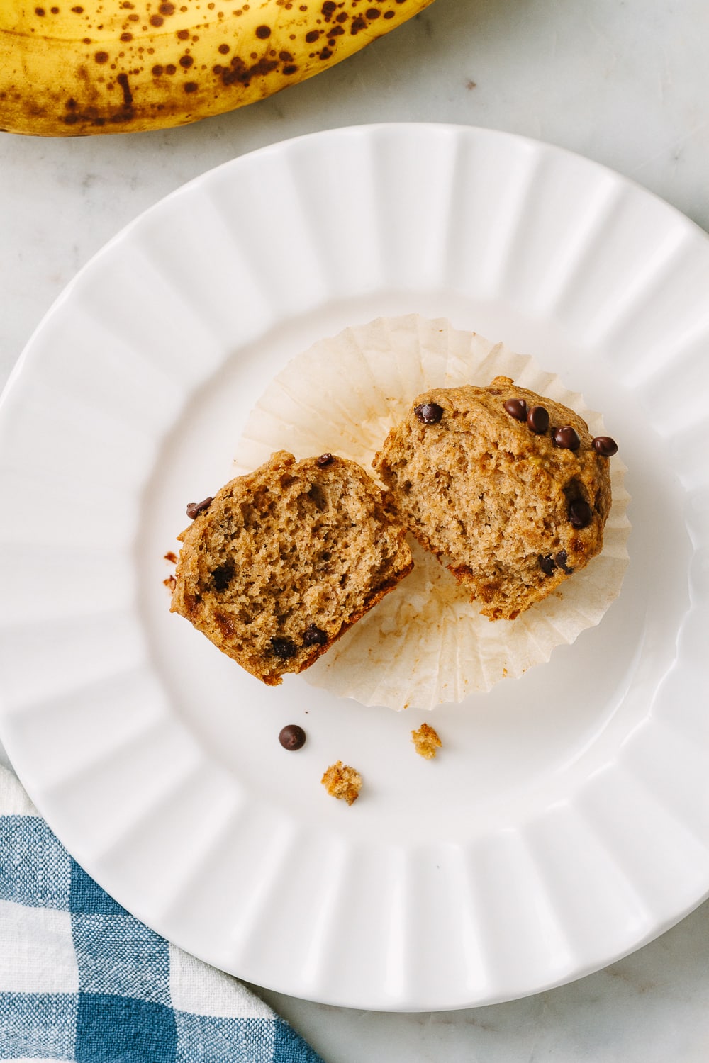 top down view of a vegan banana chocolate chip muffin pulled apart and laying on small white plate.