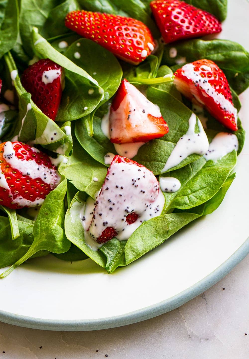 small plate with a spinach-strawberry salad topped with creamy vegan poppy seed dressing.