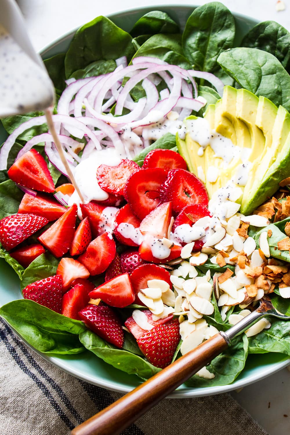 action shot of strawberry spinach salad with avocado and poppy seed dressing drizzled overtop.