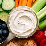 up close, top down view of a vegan cream cheese and bagel platter with veggies and fruit.