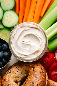 up close, top down view of a vegan cream cheese and bagel platter with veggies and fruit.