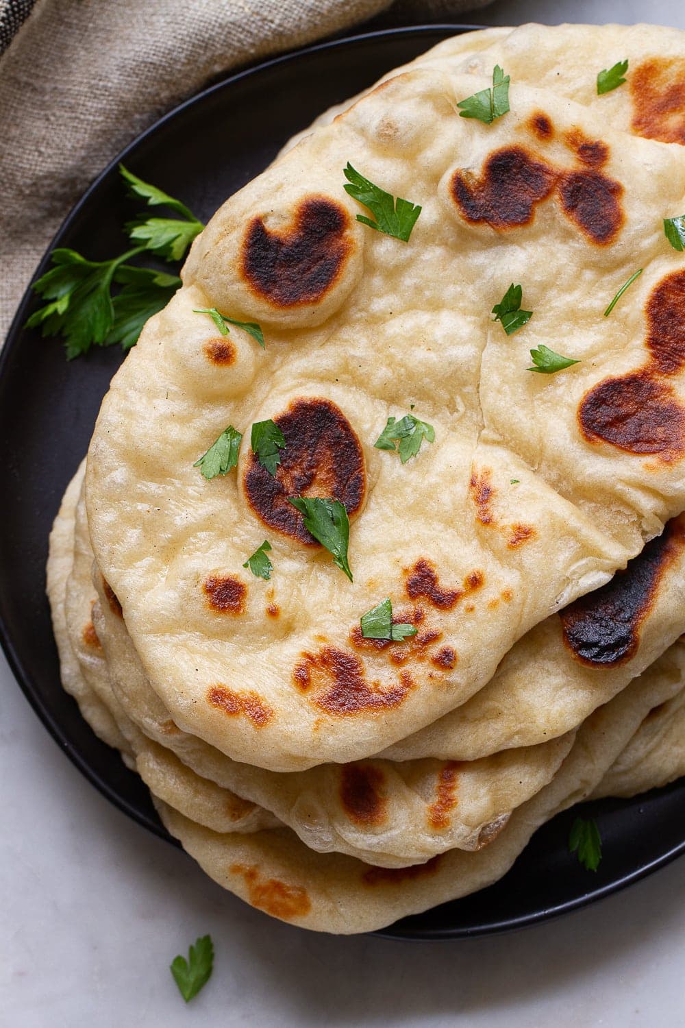 top down view of freshly made vegan naan bread stacked on a black plate.