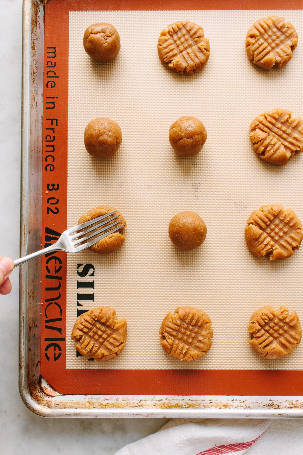 top down view of a baking sheet with vegan peanut butter cookies being pressed with a fork in criss cross pattern.