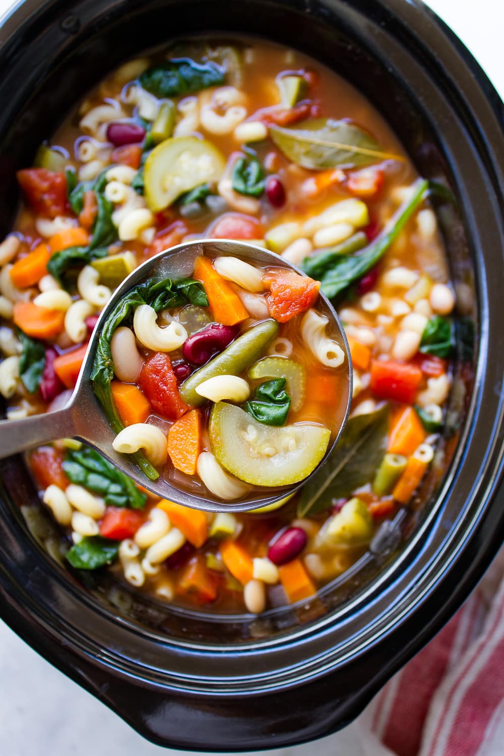 top down view of a ladle holding up a scoop full of best minestrone soup from a slow cooker dish.