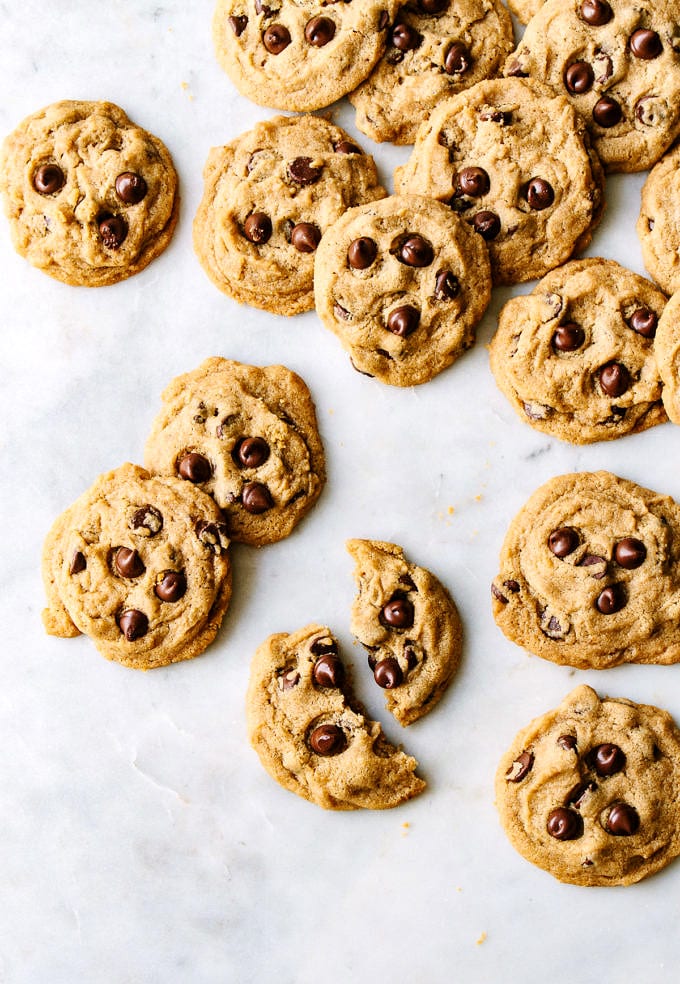 top down view of a vegan chocolate chip cookie broken in half and surrounded by a bunch of vegan chocolate chip cookies on a marble slab