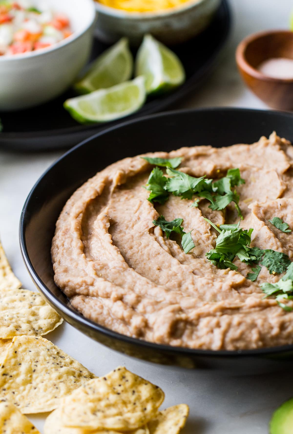 side angle view of refried beans in a black serving bowl with chopped cilantro sprinkled overtop.