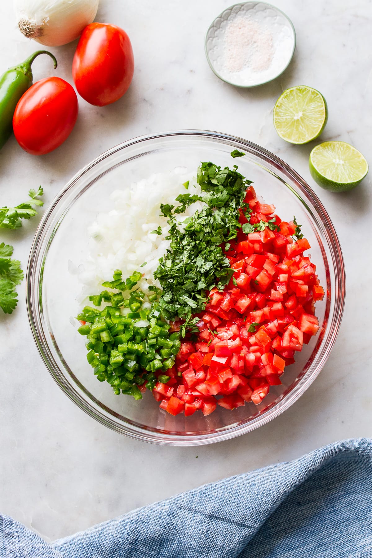 top down view of pico de gallo ingredients added to a glass mixing bowl before mixing to combine.