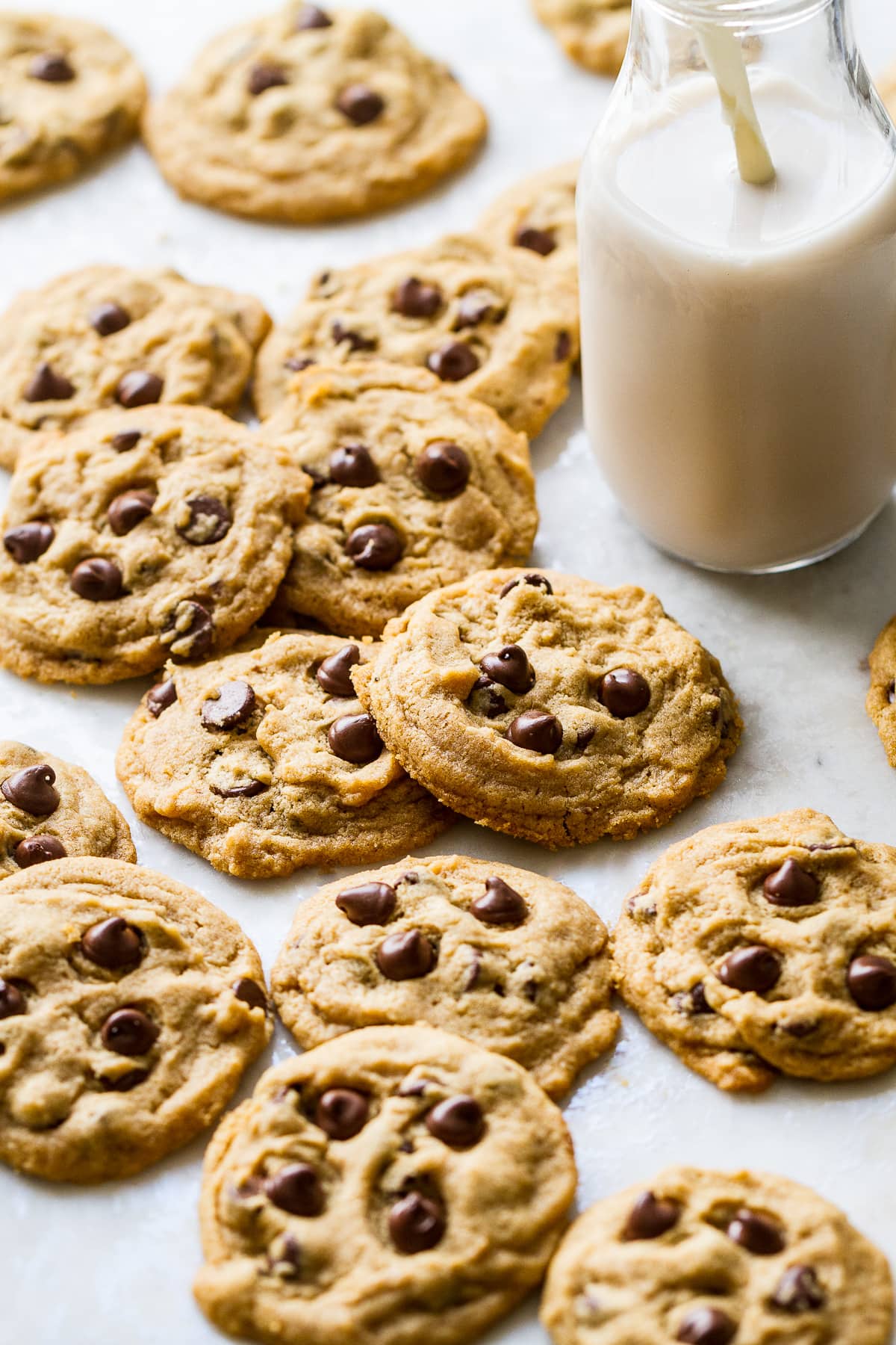 side angle view of a bunch of chocolate chip cookies laying on a marble slab with glass of almond milk nearby.