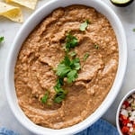 top down view of refried beans in a white serving bowl with chopped cilantro sprinkled overtop.