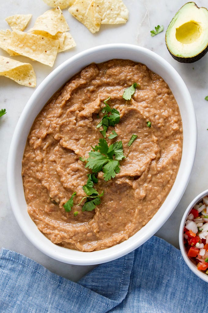 top down view of refried beans in a white serving bowl with chopped cilantro sprinkled overtop.