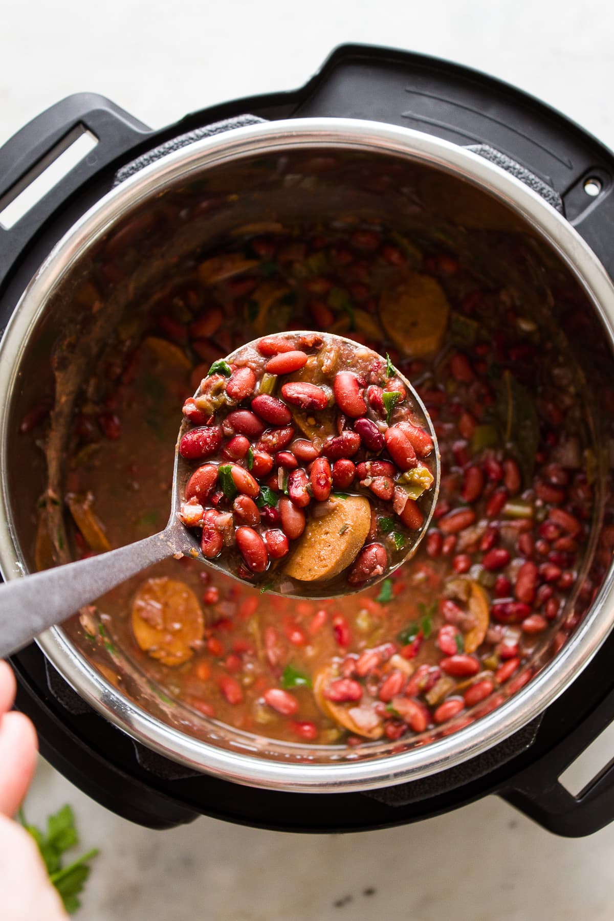 top down view of an instant pot with a ladle holding a ladle full of cajun style red beans.