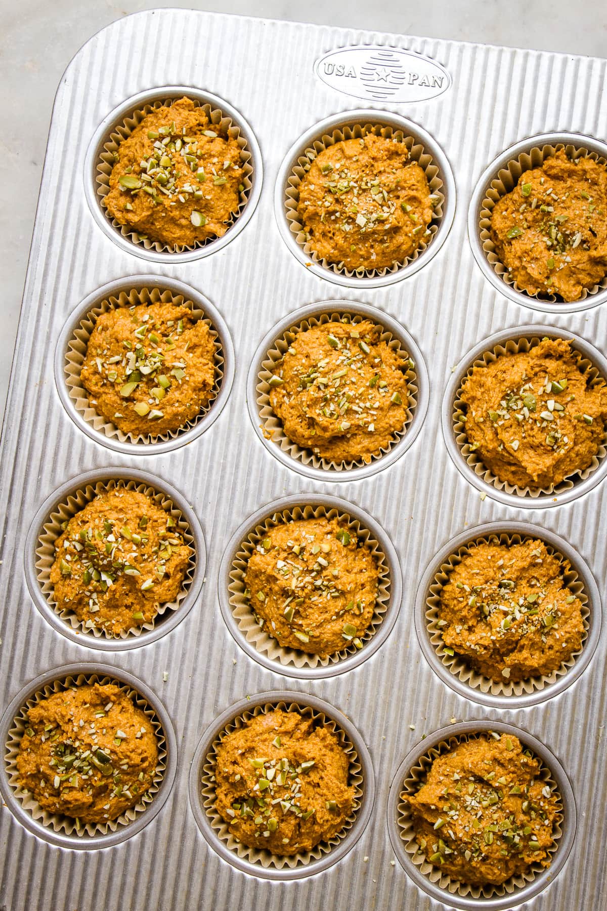 top down view of vegan pumpkin batter added to lined muffin tin and sprinkled with chopped pepitas (pumpkin seeds).