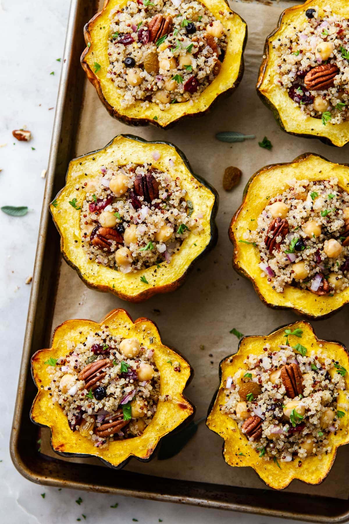 top down view of a group of stuffed acorn squash with quinoa, cranberries and chickpeas on a baking sheet.