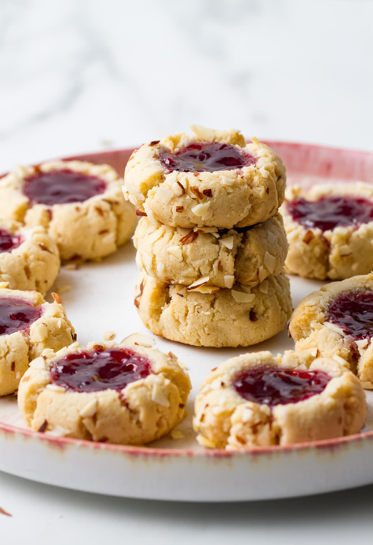 head on view of 3 stacked almond thumbprint cookies surrounded by more cookies.