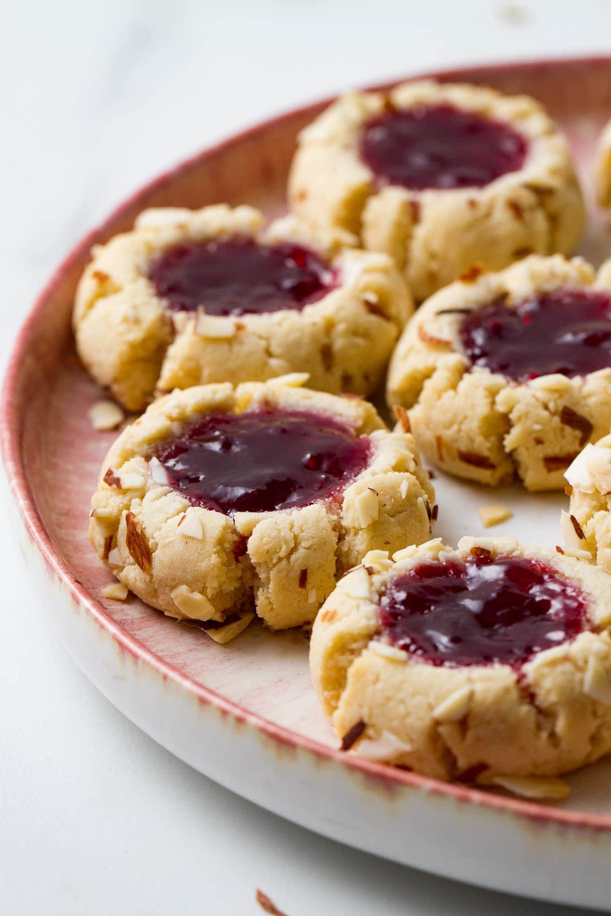 side angle view of freshly made almond flour thumbprint cookies on a small pink and white plate.