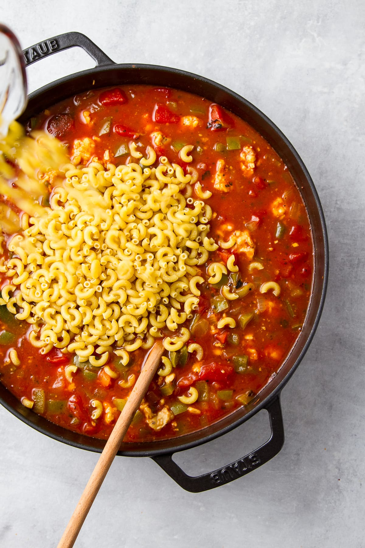 top down view showing uncooked pasta poured into pot of vegan goulash to cook until tender.