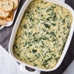 top down view of prepared vegan spinach artichoke dip with items surrounded.