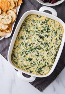 top down view of prepared vegan spinach artichoke dip with items surrounded.