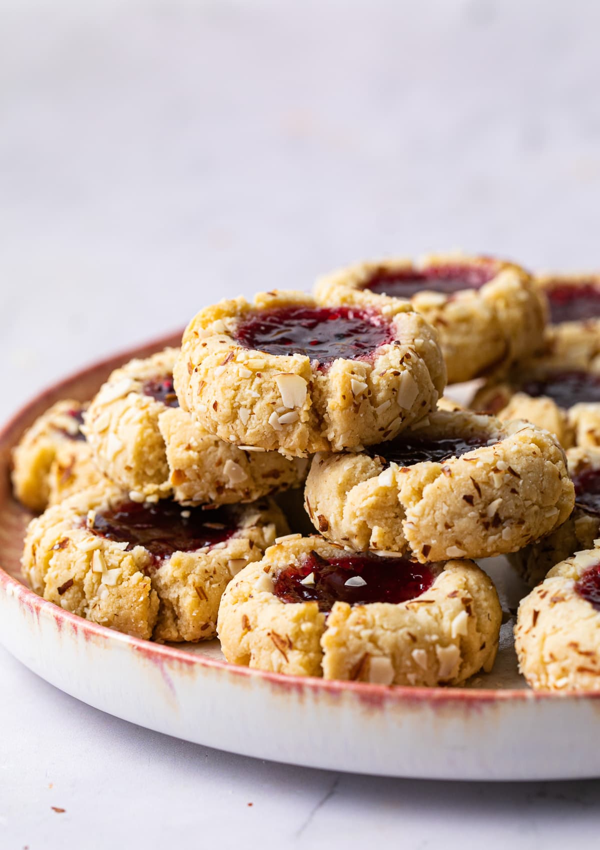 head on view of stacked almond thumbprint cookies surrounded by more cookies.