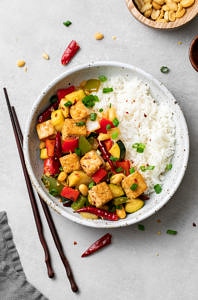 top down view of a serving of kung pao tofu and rice in a bowl with things surrounding.