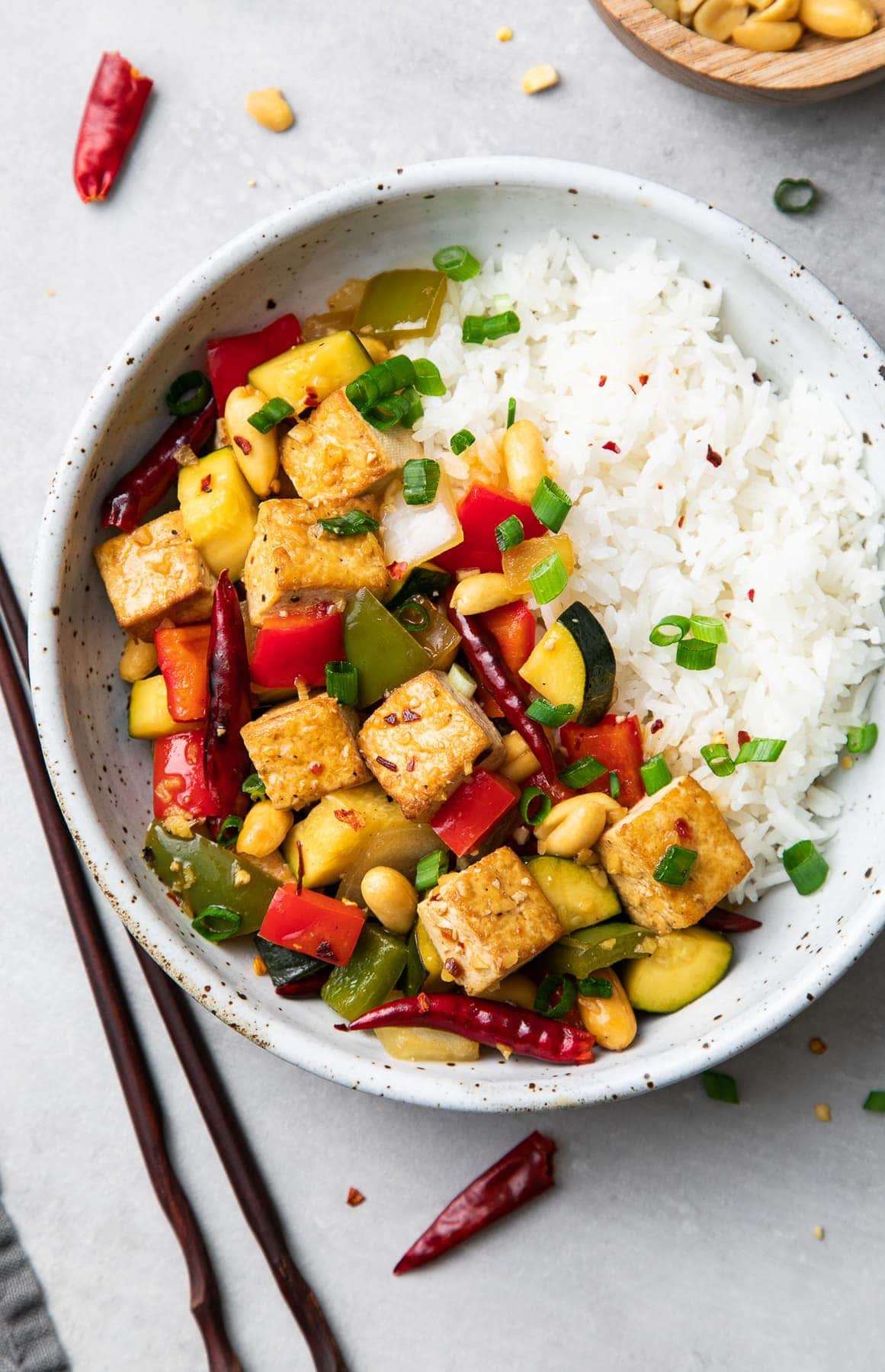 top down view of a serving of kung pao tofu and rice in a bowl with things surrounding.