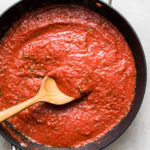 top down view of freshly made batch of homemade marinara sauce in a pan with wooden spoon.