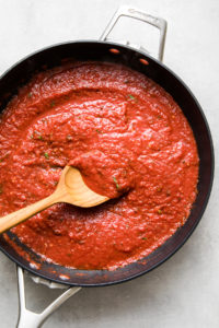 top down view of freshly made batch of homemade marinara sauce in a pan with wooden spoon.