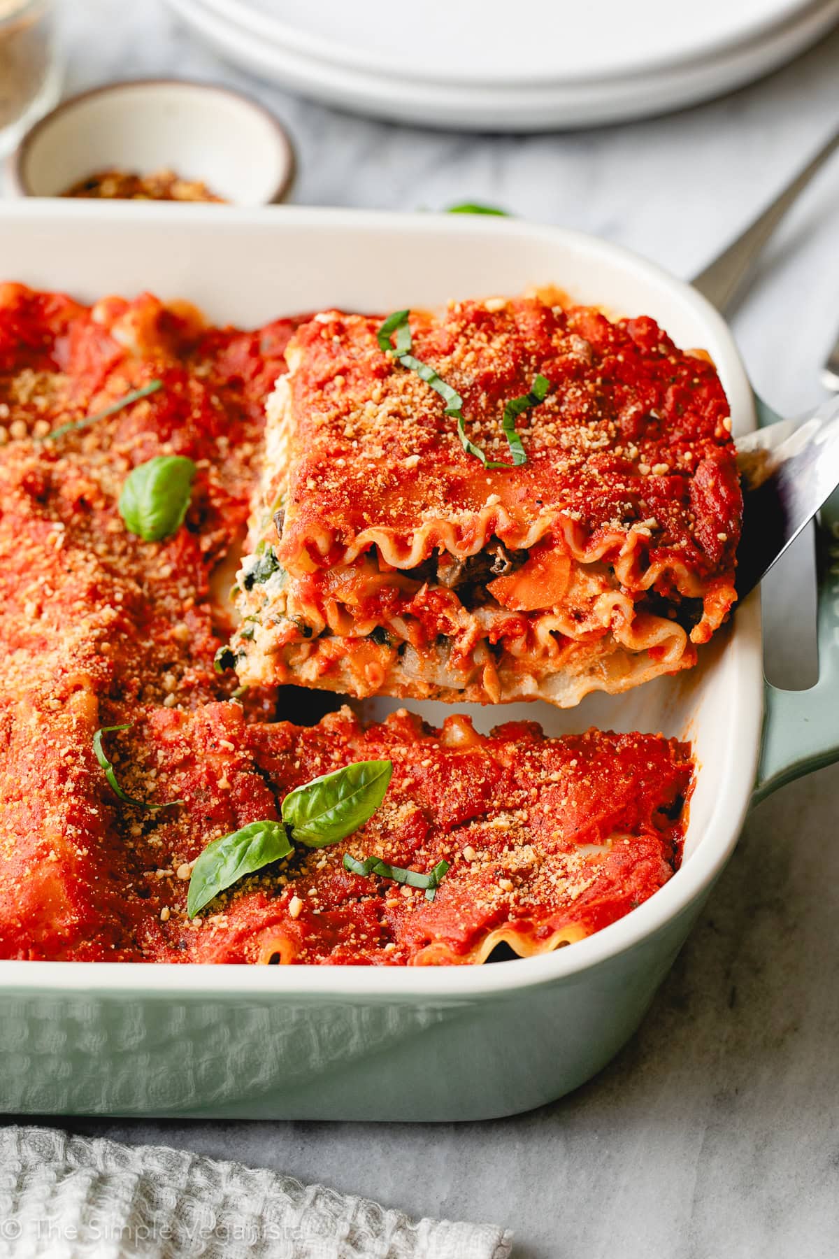 side angle view of a hearty slice of vegan lasagna served in a baking dish, garnished with fresh basil leaves.