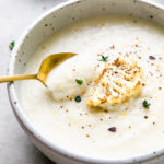 side angle view of creamy vegan cauliflower soup with spoon and items surrounding.